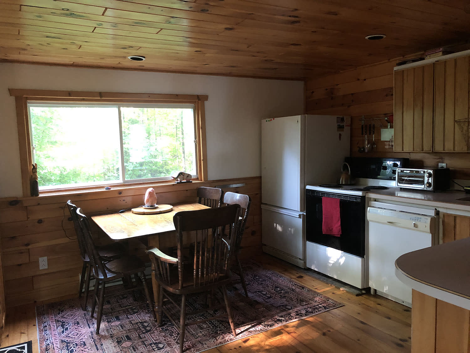 In a wood paneled room, a small dining set next to a wall of white kitchen appliances