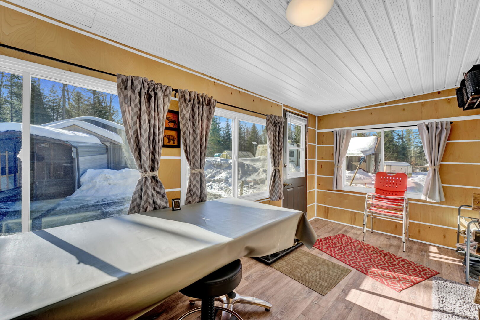 A covered table with a stood beneath it in a wood-paneled sunroom