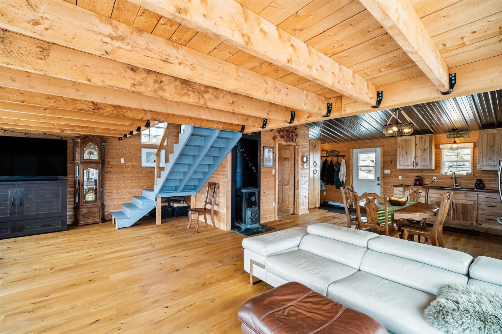 Exposed beam ceiling and bright wood floors with a blue staircase and artisan stove