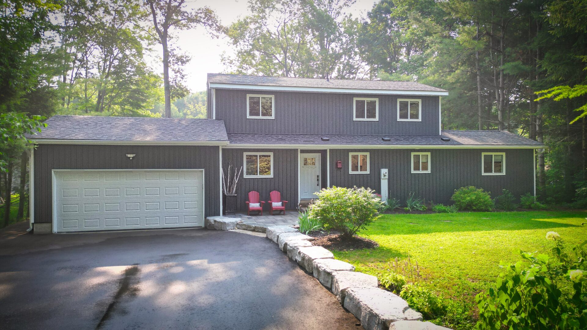 A blue-grey cottage with white trim and a long paved driveway