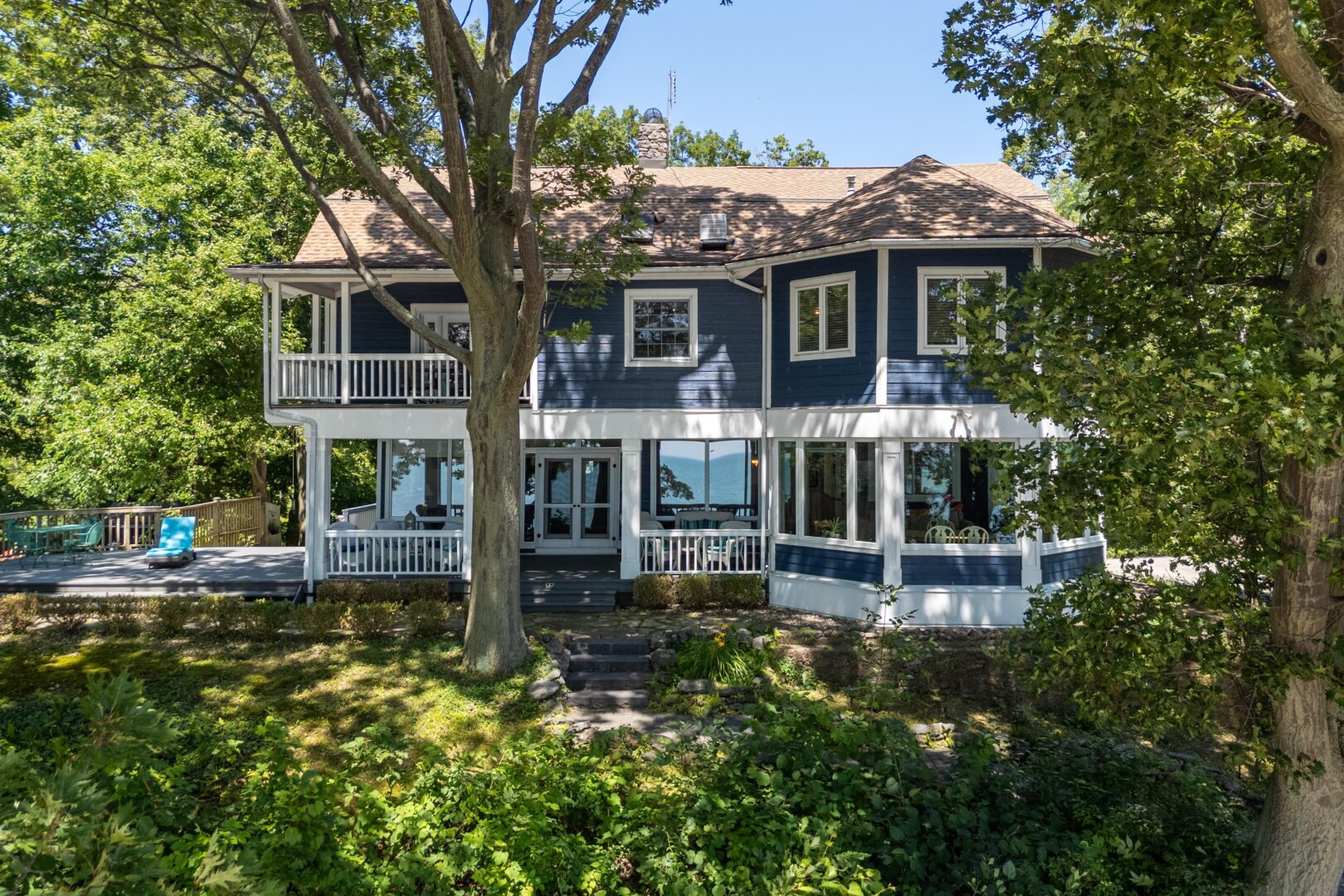 Grand view of the historic Seven Oaks home from the lakeside, surrounded by trees and featuring wraparound porches