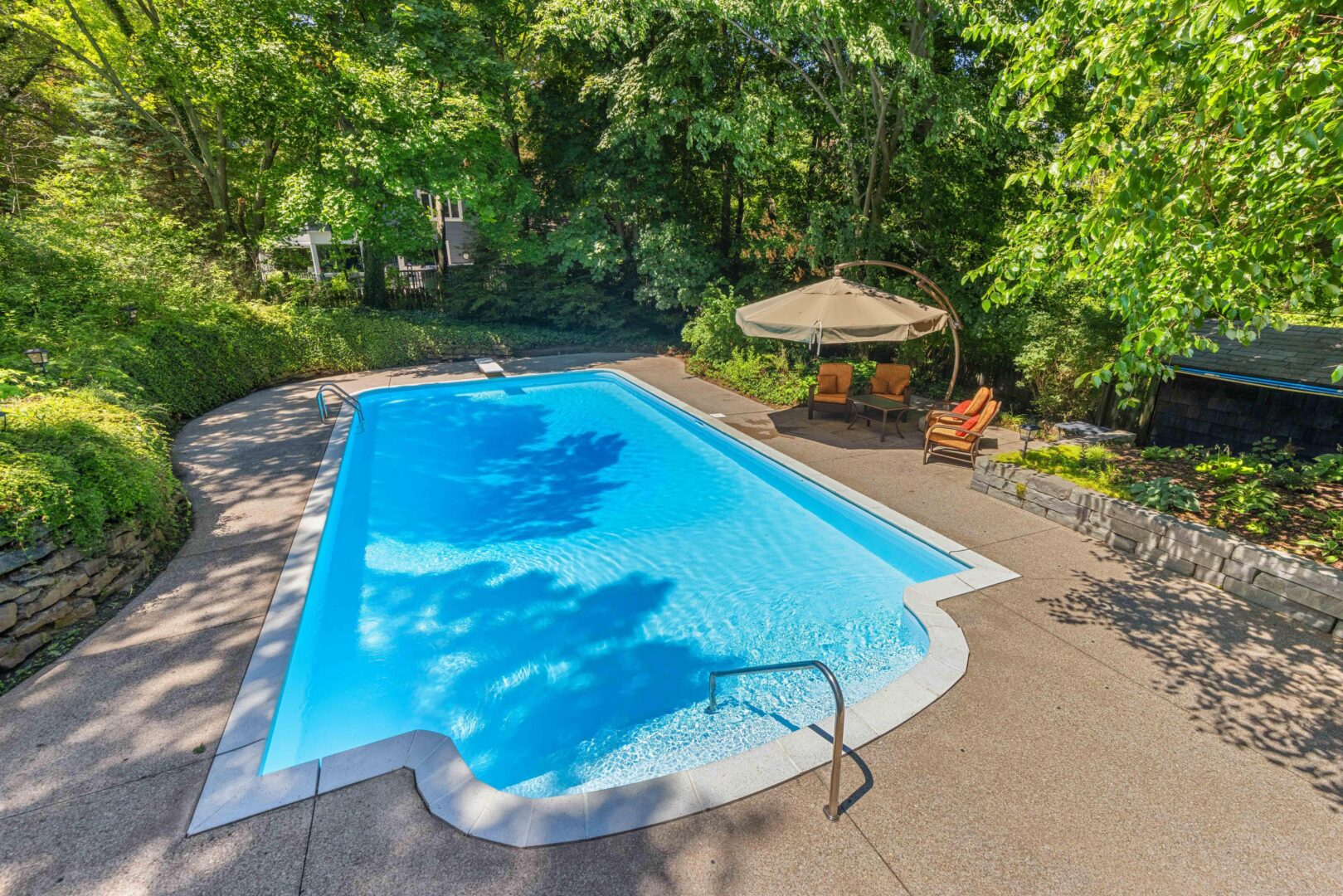 Spacious in-ground pool nestled in a private stone patio surrounded by trees and lounge seating