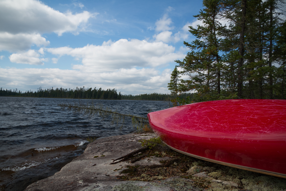 Red tandem canoe upside down on a rocky shore