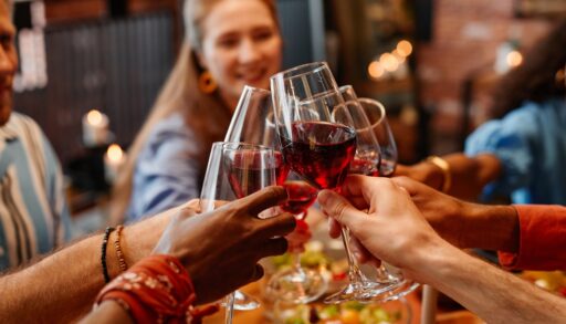 Close up of young people holding wine glasses and toasting while celebrating together at table during dinner party, hangover
