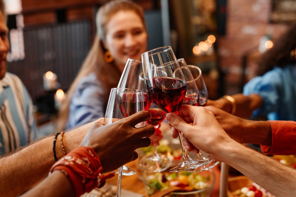 Close up of young people holding wine glasses and toasting while celebrating together at table during dinner party, hangover