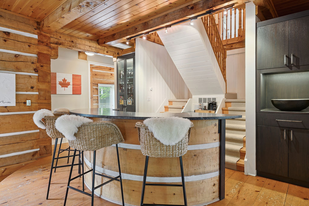 A half-moon shaped pale wood bar with two high-top chairs in a wood paneled room