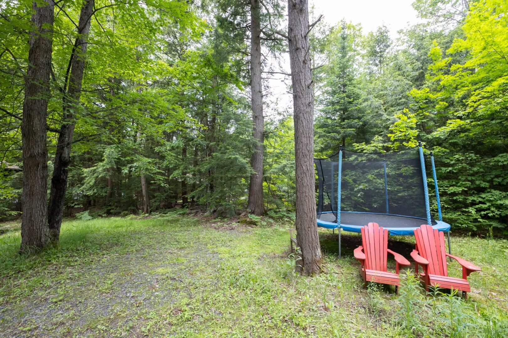 A trampoline and red Muskoka chairs on a grassy lawn