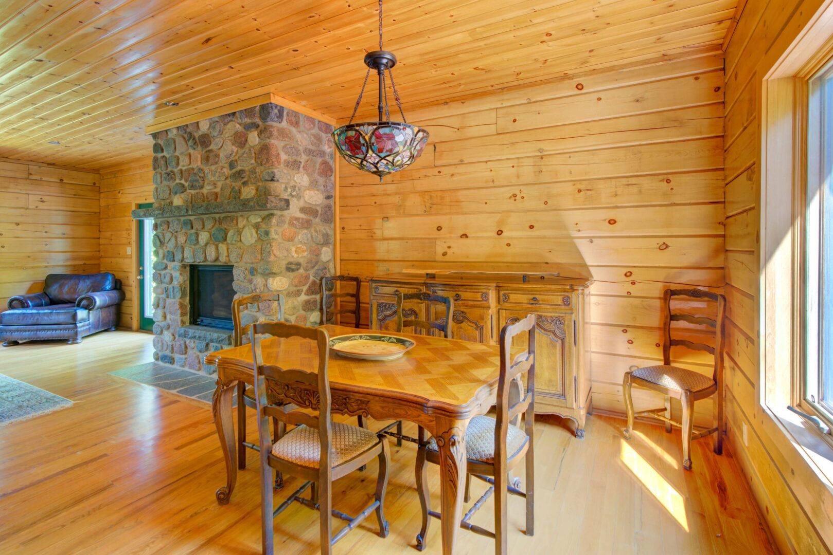 A wood dining table next to a stone fireplace in a wood paneled room