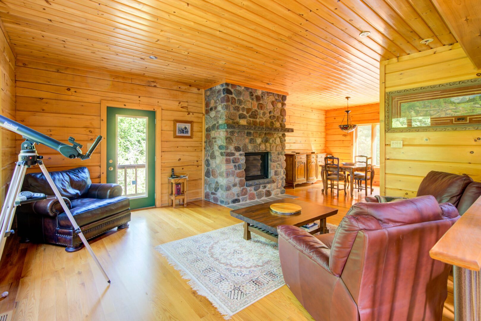 Brown leather couches face a stone fireplace in a wood paneled room