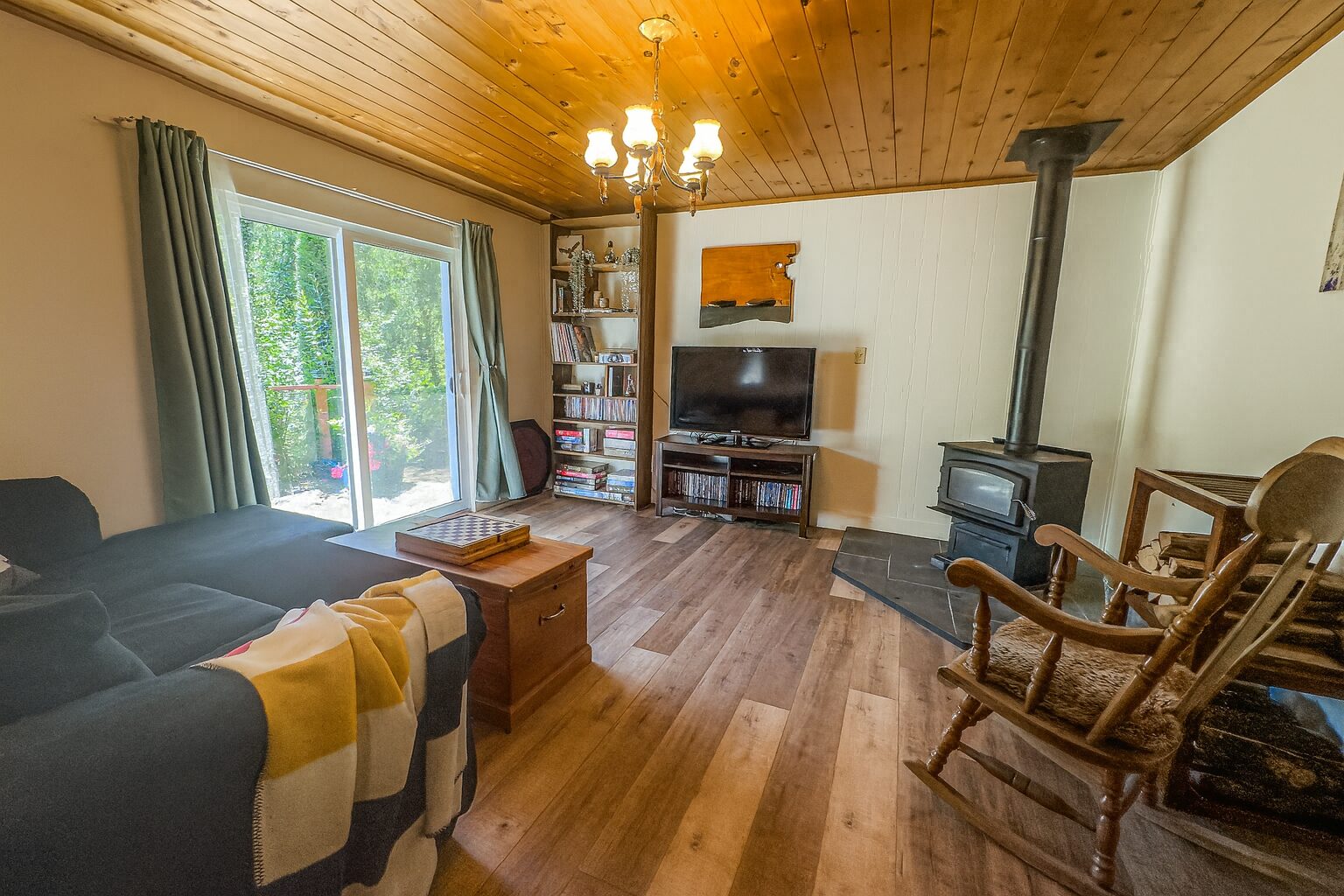 A living room with wood floors and a wood ceiling. A wood stove sits in the right corner