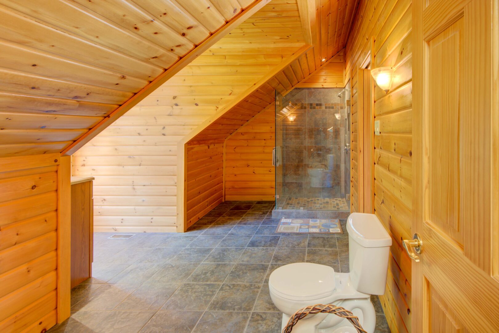 A stone walk-in shower with glass walls in a wood paneled bathroom