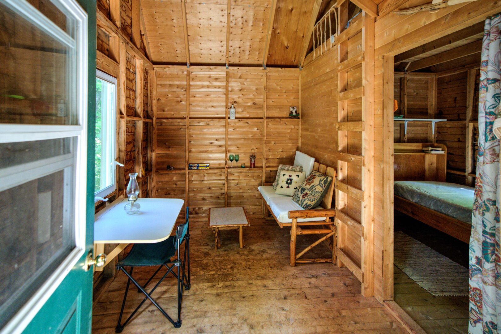 A wood bunkie interior with a small table and wood ladder steps to a loft