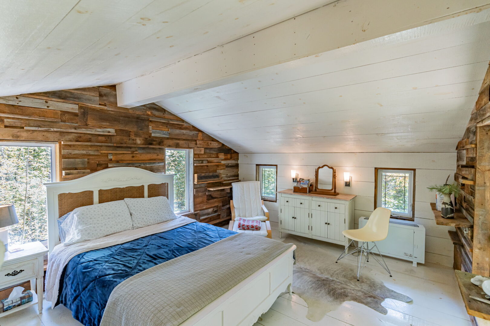 Bright bedroom with sloped ceiling, reclaimed wood accent wall, and white painted floors inside rustic log guest cabin