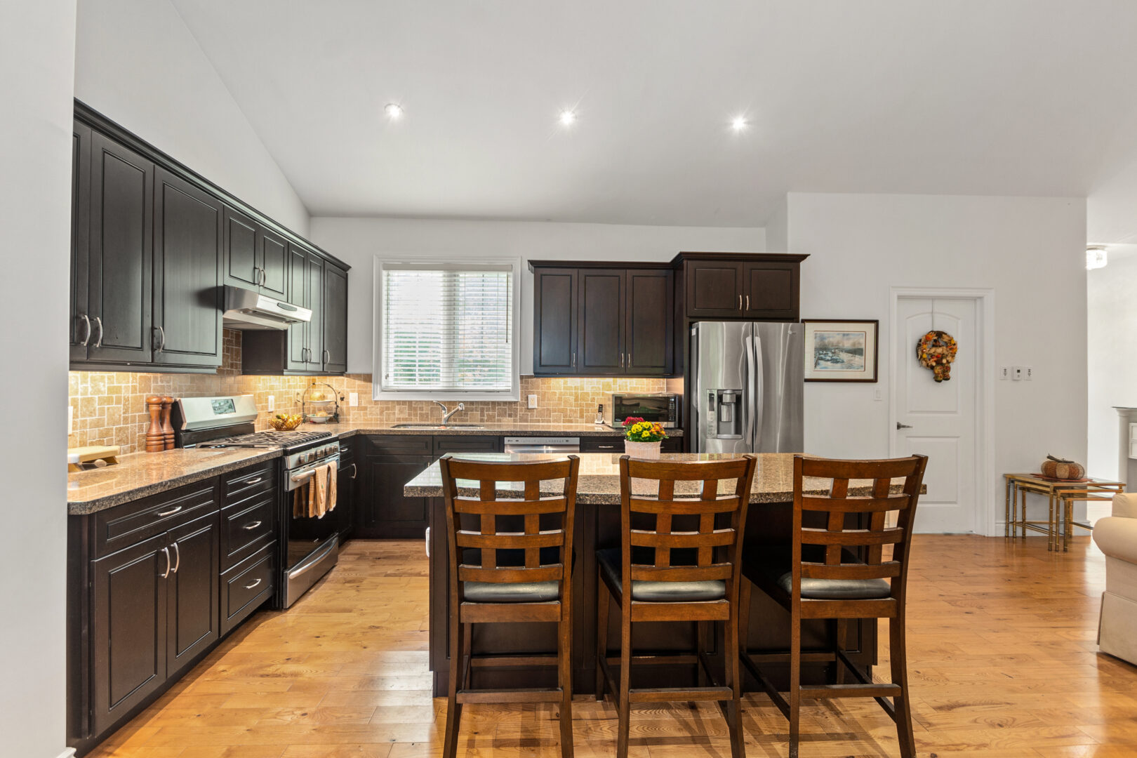 A kitchen island with three high-top chairs faces a sink and fridge