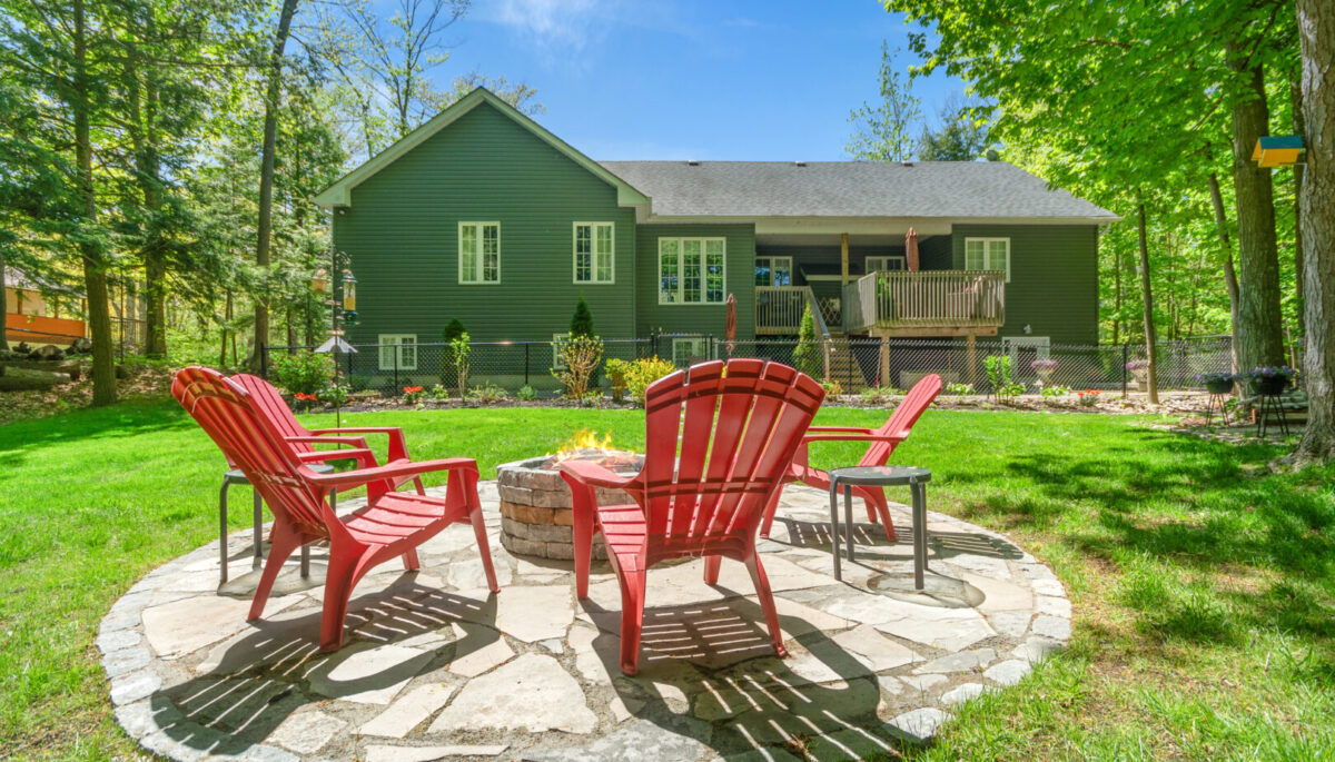 Red Muskoka chairs on a round stone patio in a backyard