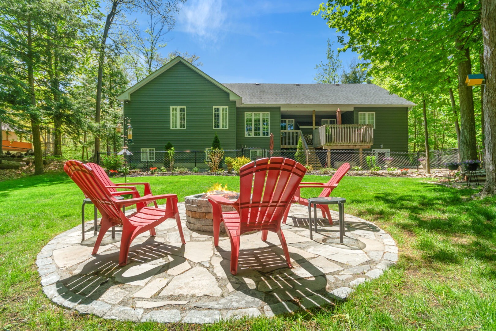 Red Muskoka chairs on a round stone patio in a backyard