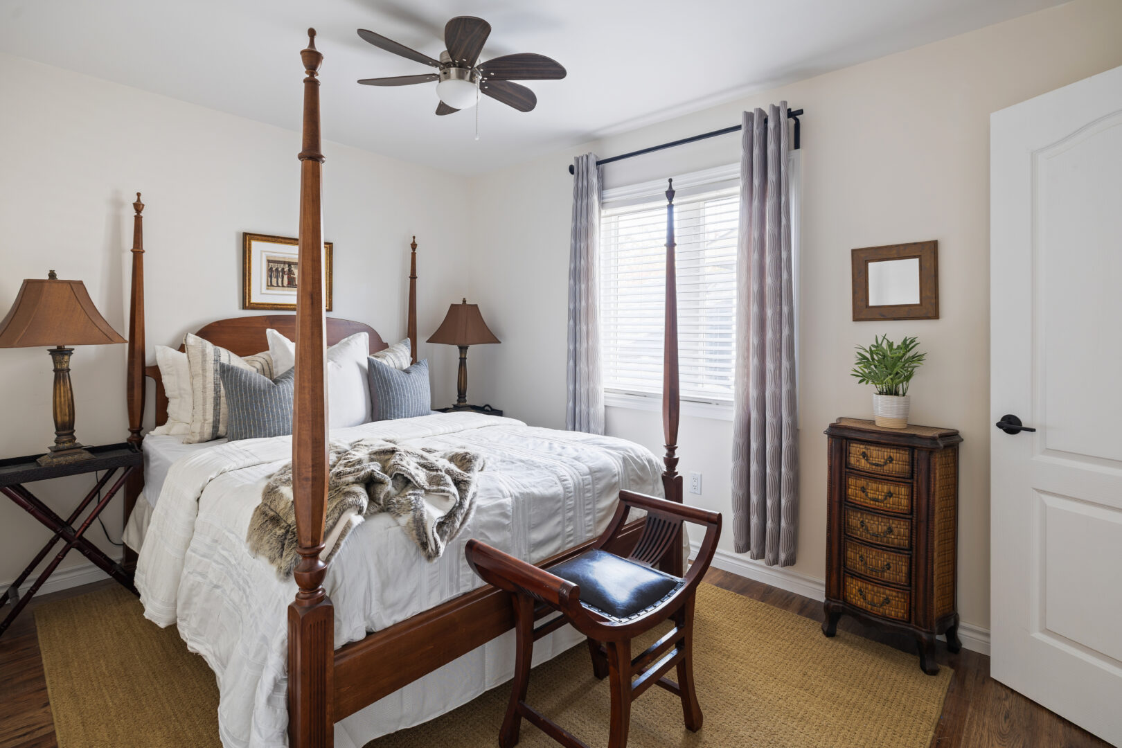 A white bed on a brown bed frame with tall bed posts in a white bedroom