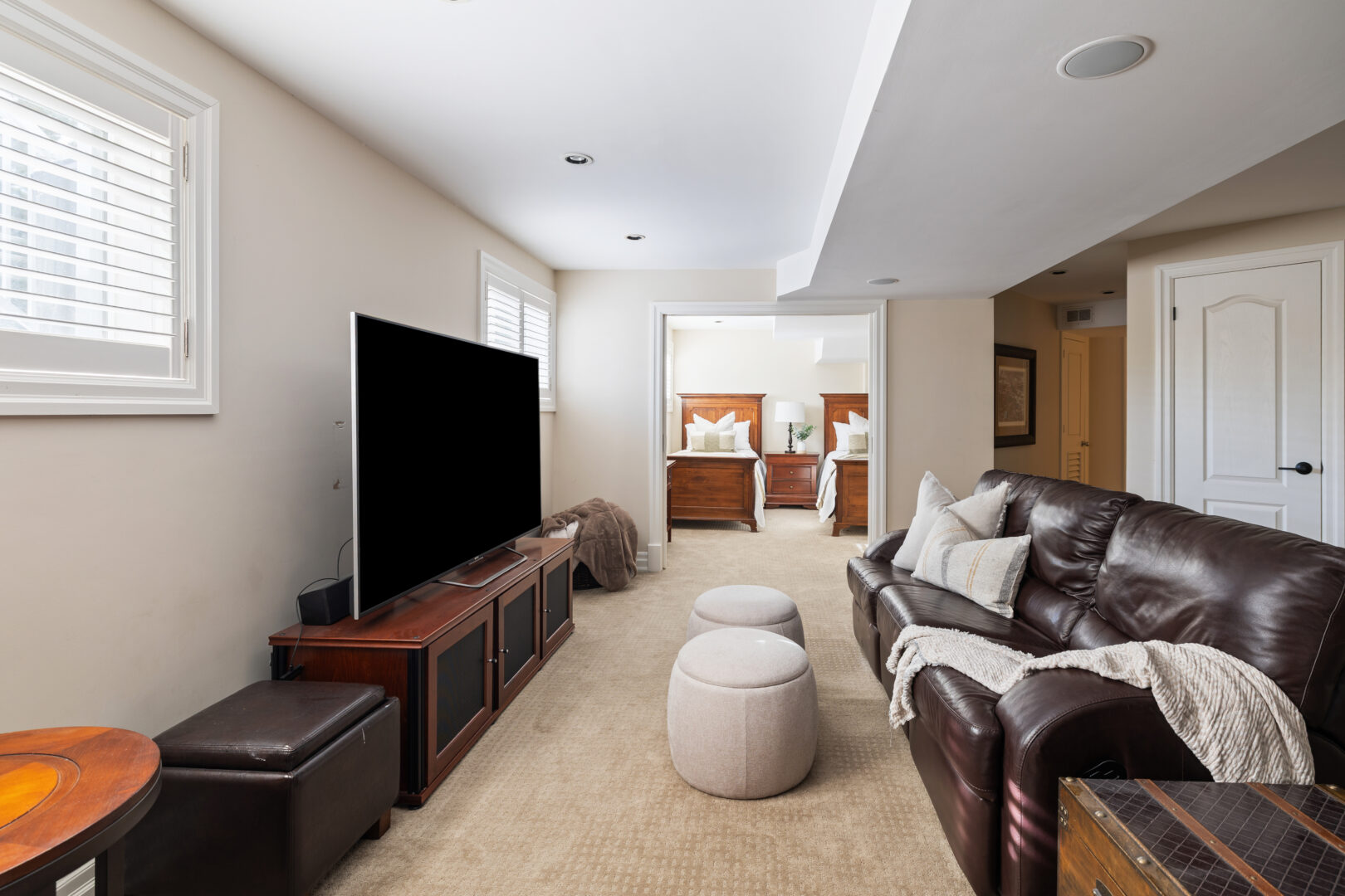 A finished basement with beige carpeting. A grey couch faces a flat screen TV