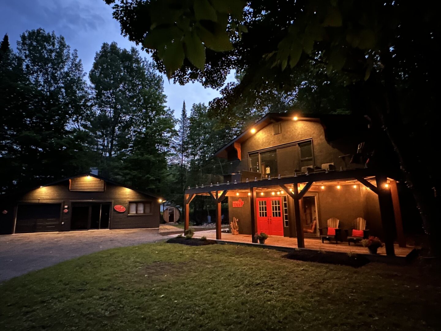 A wood cottage with red Muskoka chairs in the front is lit up by fairy lights at night