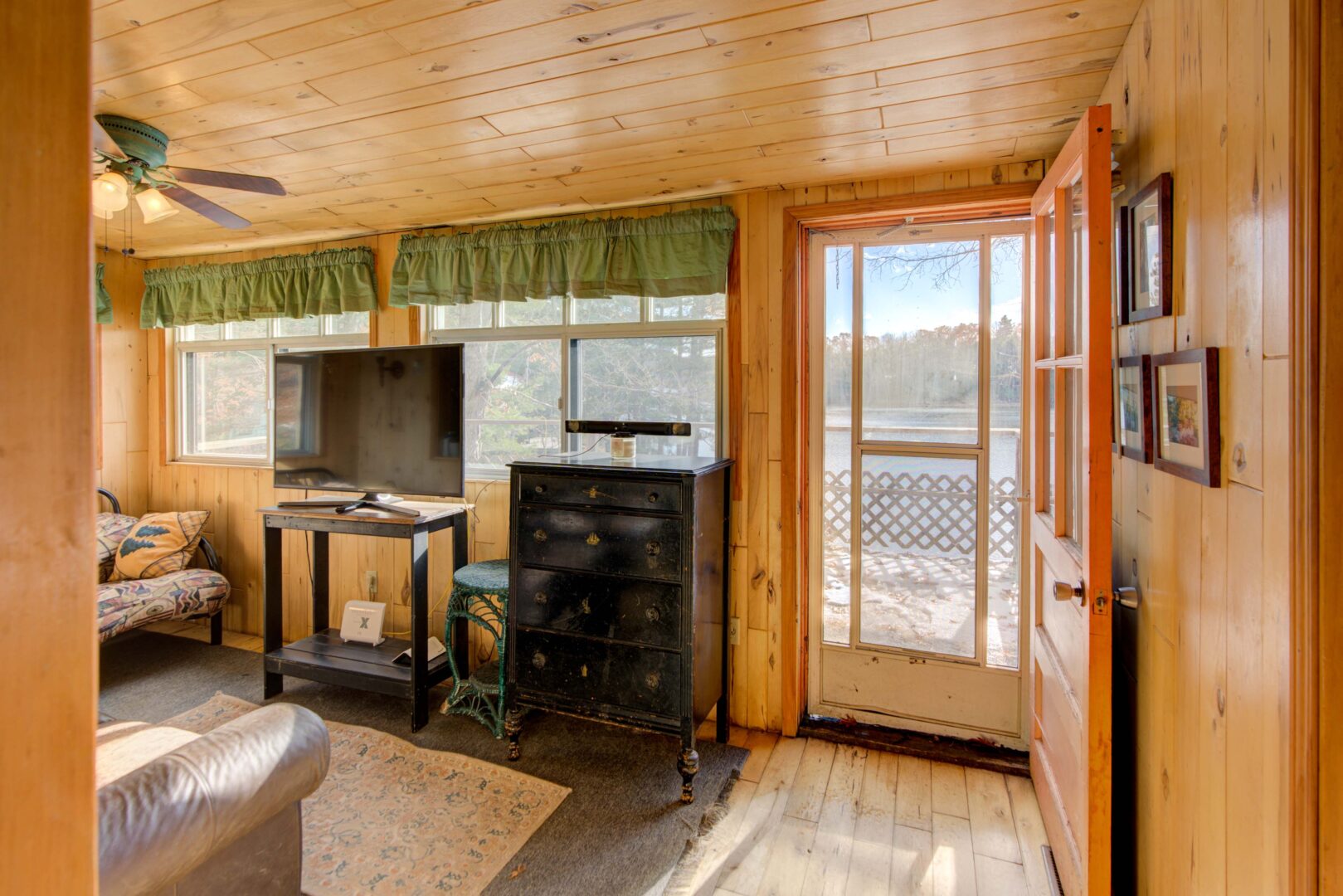 A black cabinet and a TV on a window-lined wall. to the right, a screen door