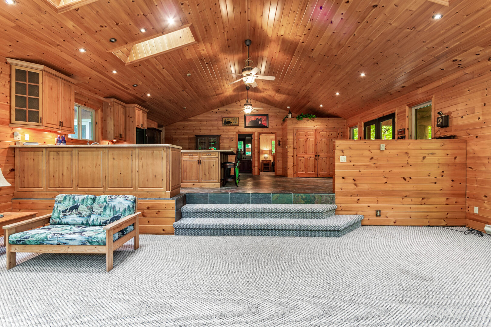 An empty carpeted living area with steps leading up into the kitchen