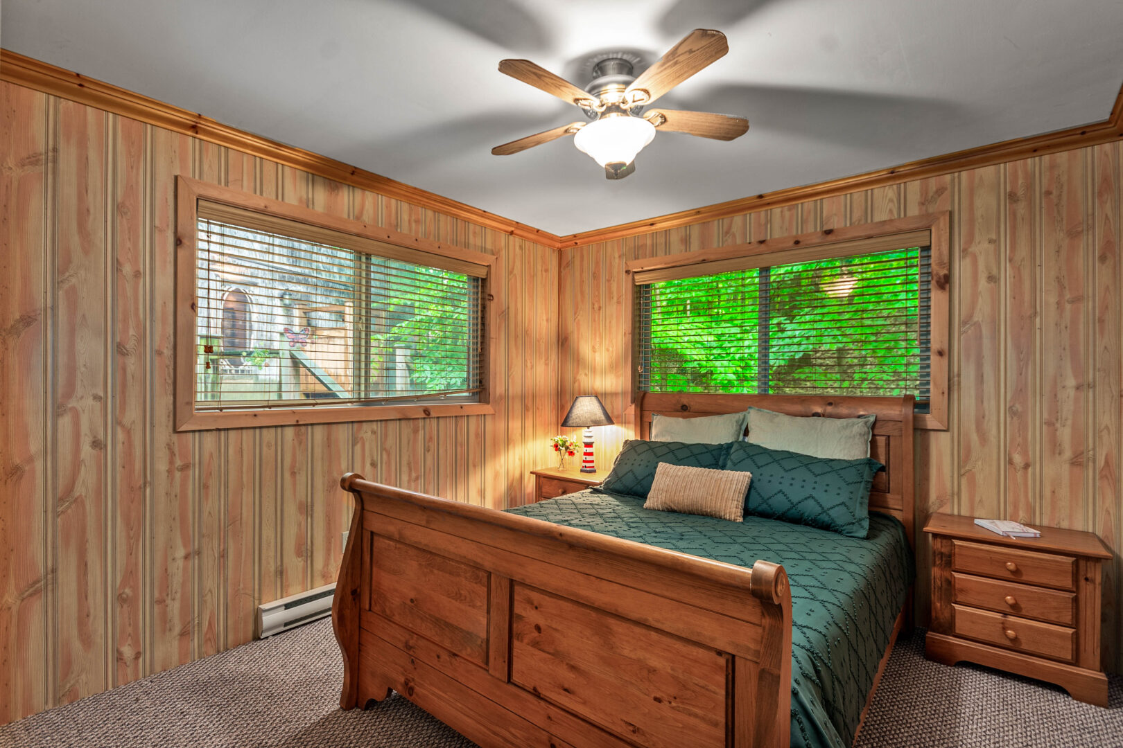 A wood paneled room with a wood sled bed with green bedding