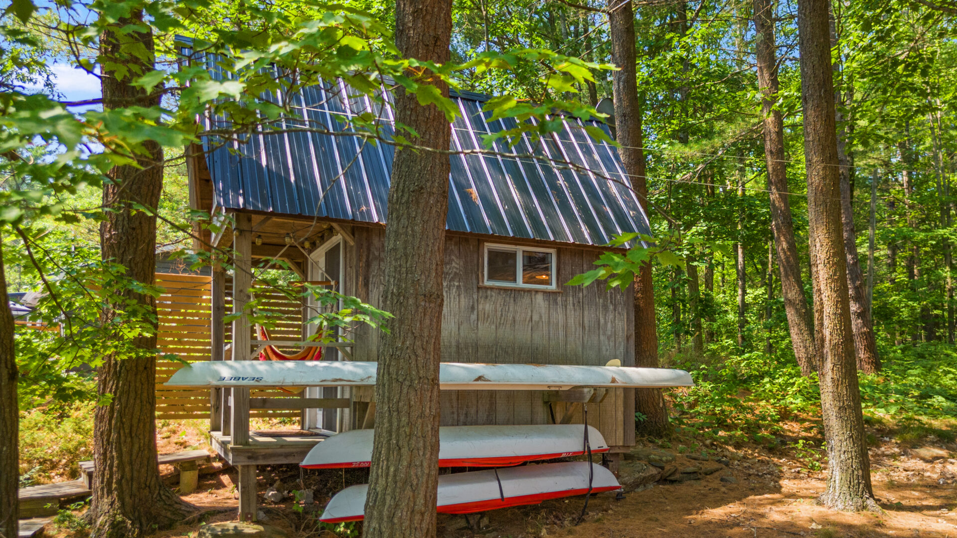 A small wood cabin with a blue roof. Next to it, paddleboards are stacked