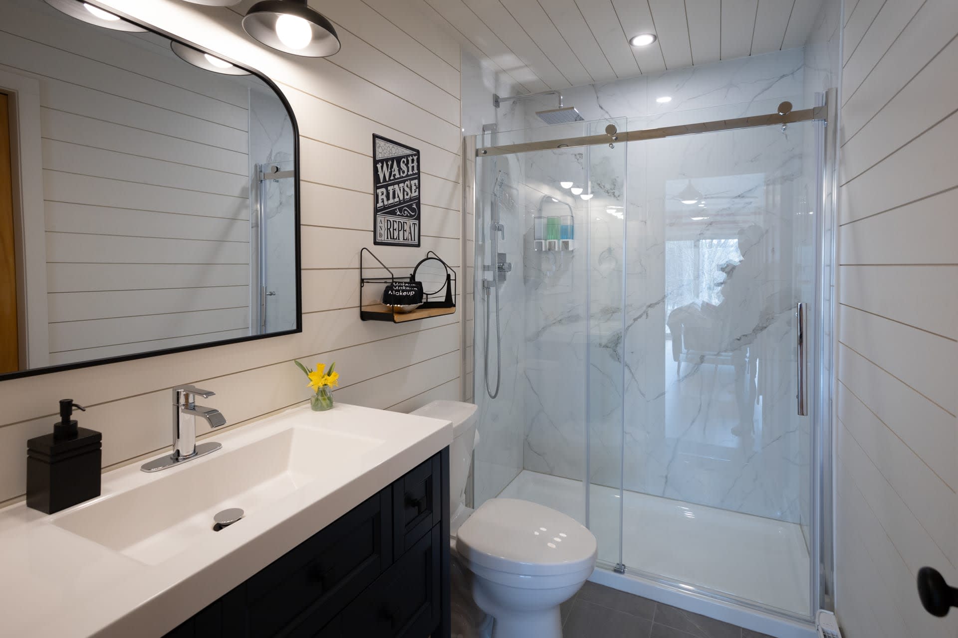 A white bathroom with a dark blue vanity and a glass shower