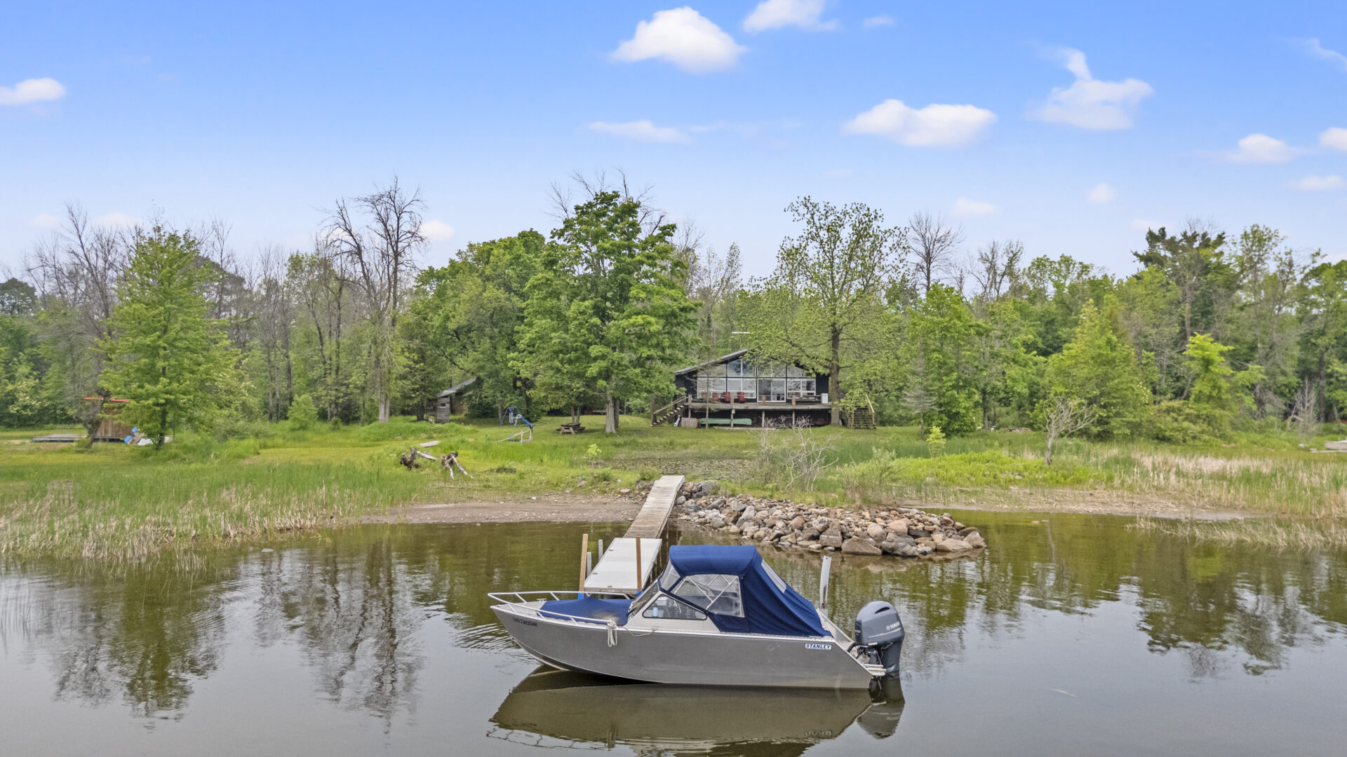 A cottage nestled on a cottage property. A boat is parked at the end of a dock