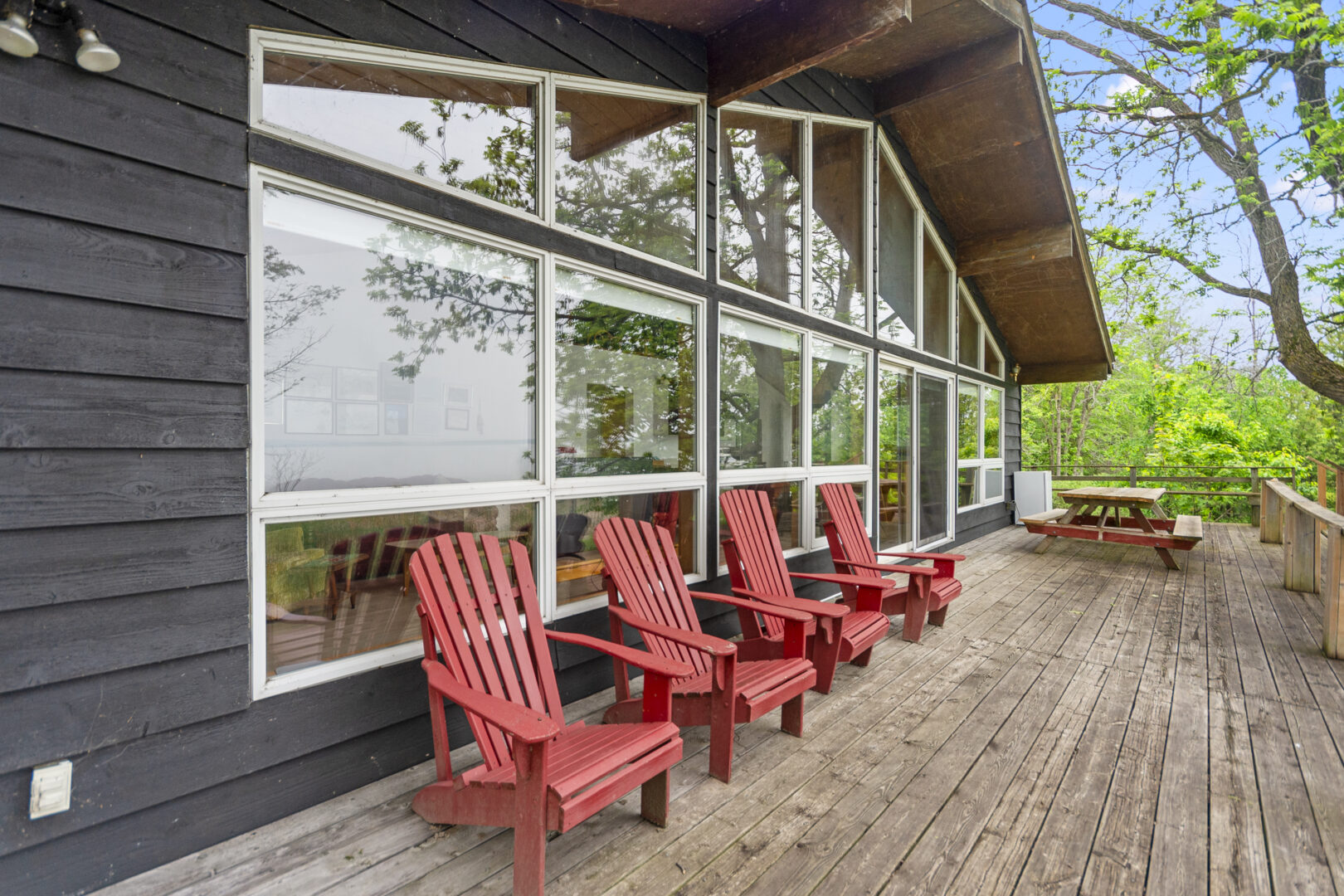 A wood deck along the back of a cottage with red Muskoka chairs