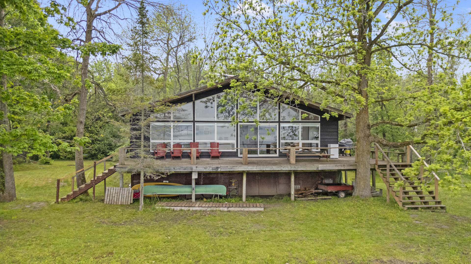 A cottage with a wall of a windows and balcony with red Muskoka chairs