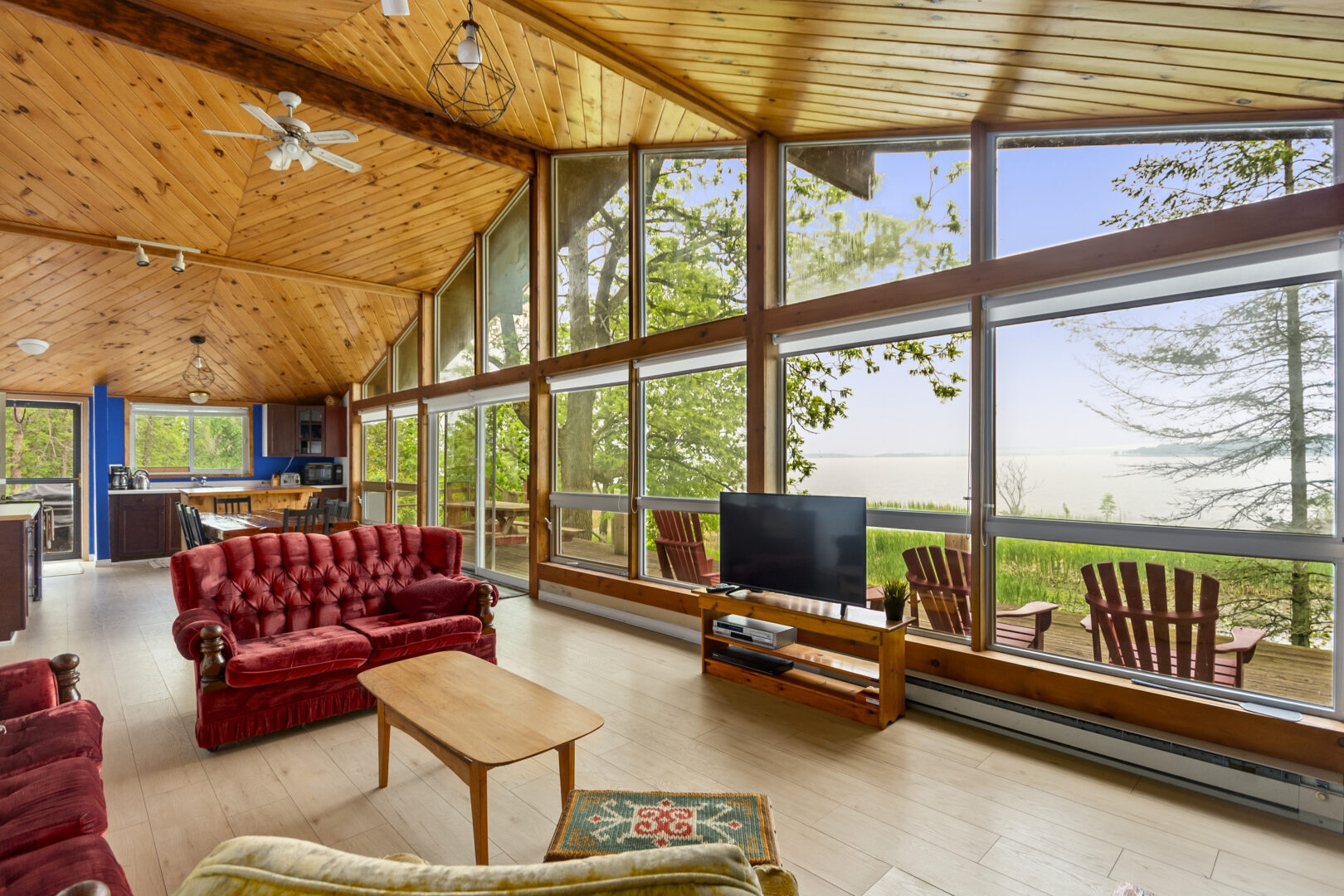 Red couches face a TV in bright living room with cathedral ceilings and floor-to-ceiling windows