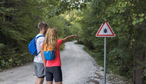 Two people pointing at a sign for ticks
