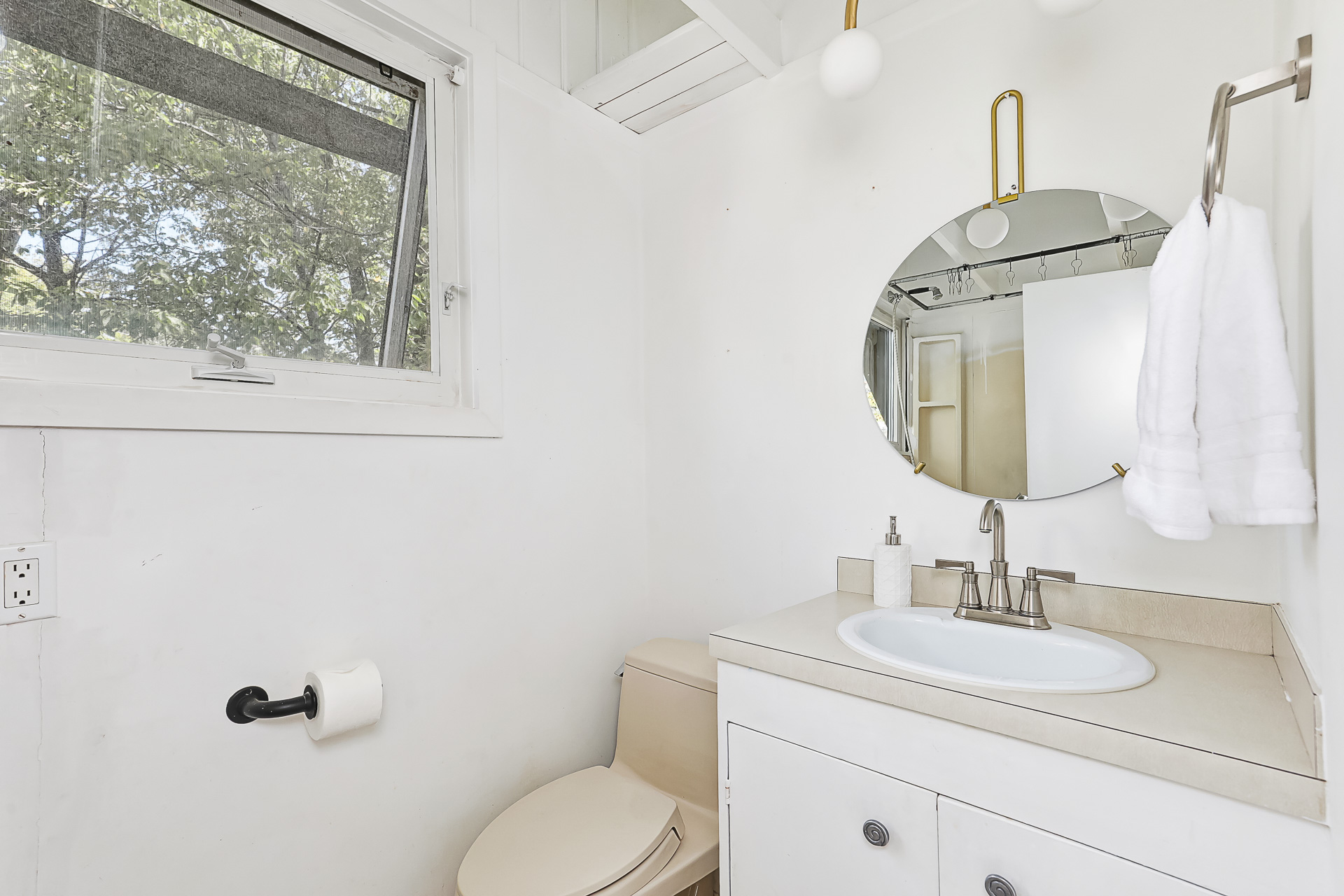 A white bathroom with a round mirror above the white vanity