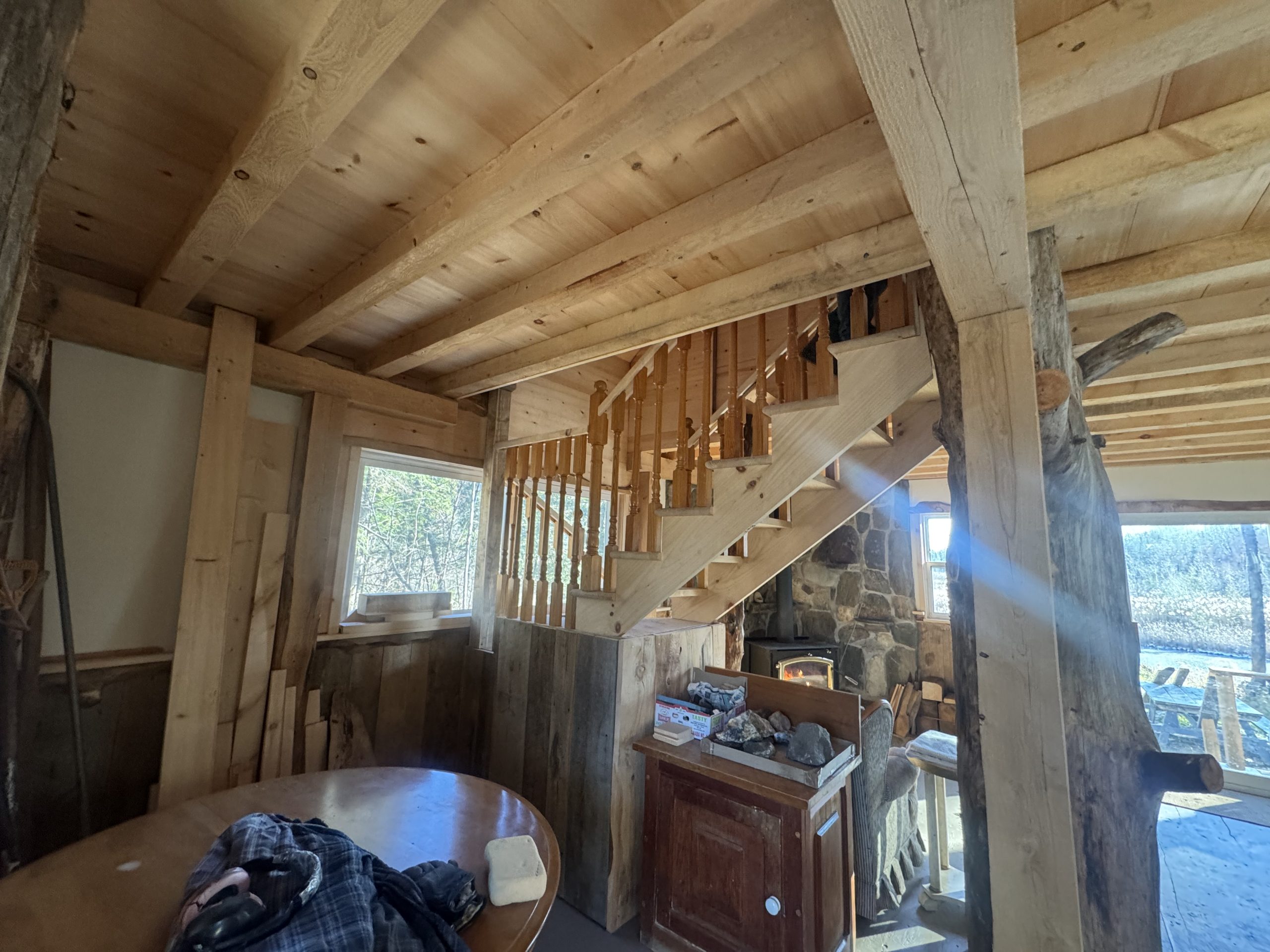 A round wood table tucked under wood steps that lead upstairs