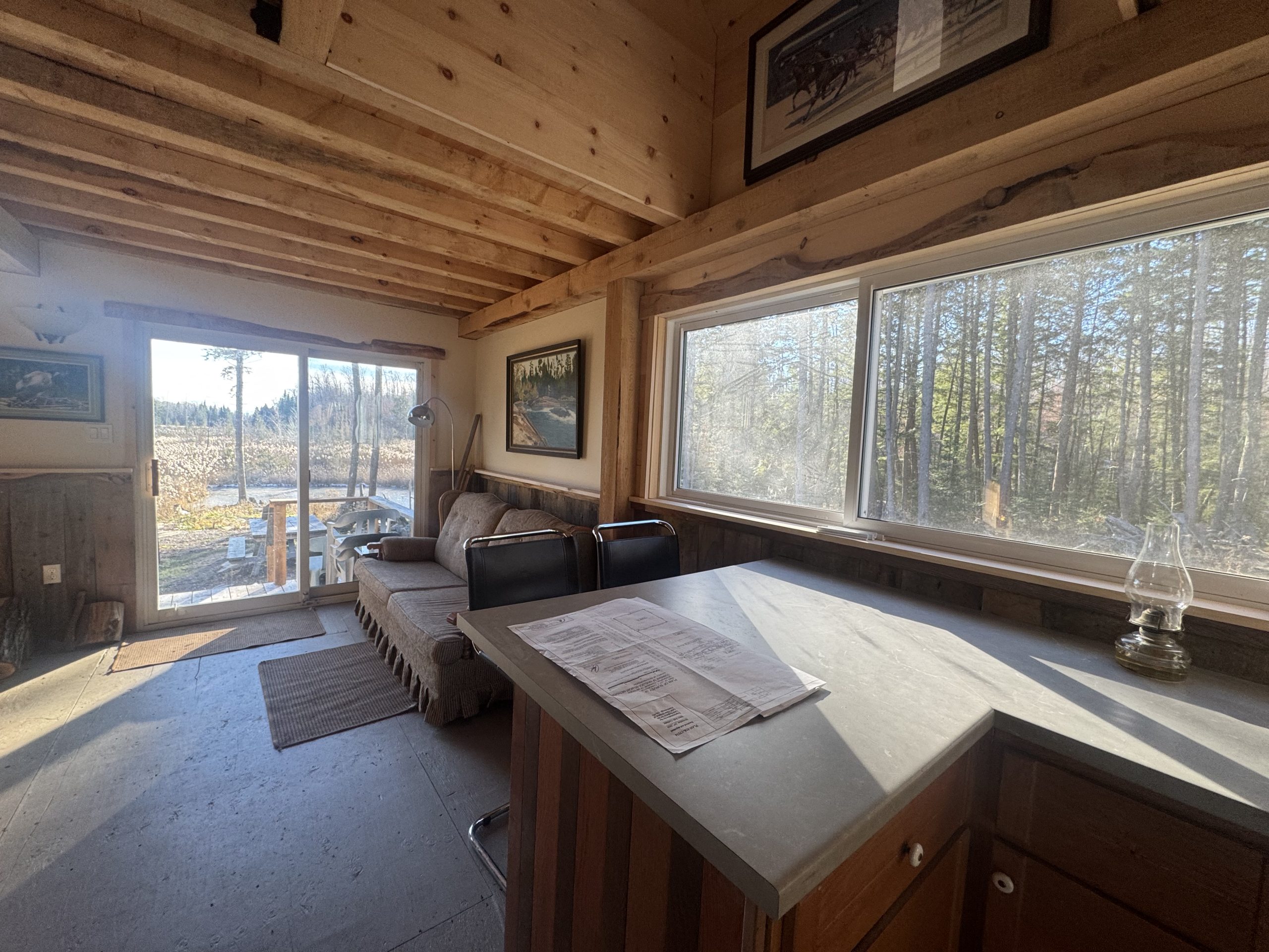 The interior of a wood cabin with bright windows. A kitchen counter faces a beige couch