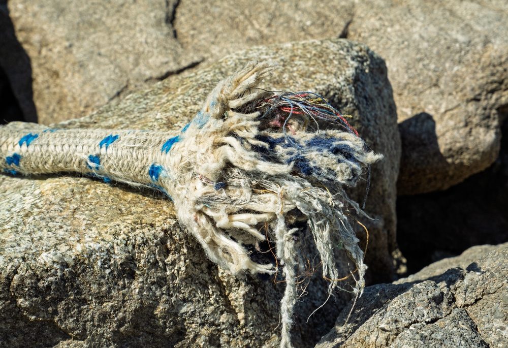 Close-up of a frayed end of a boating rope sitting on a rock