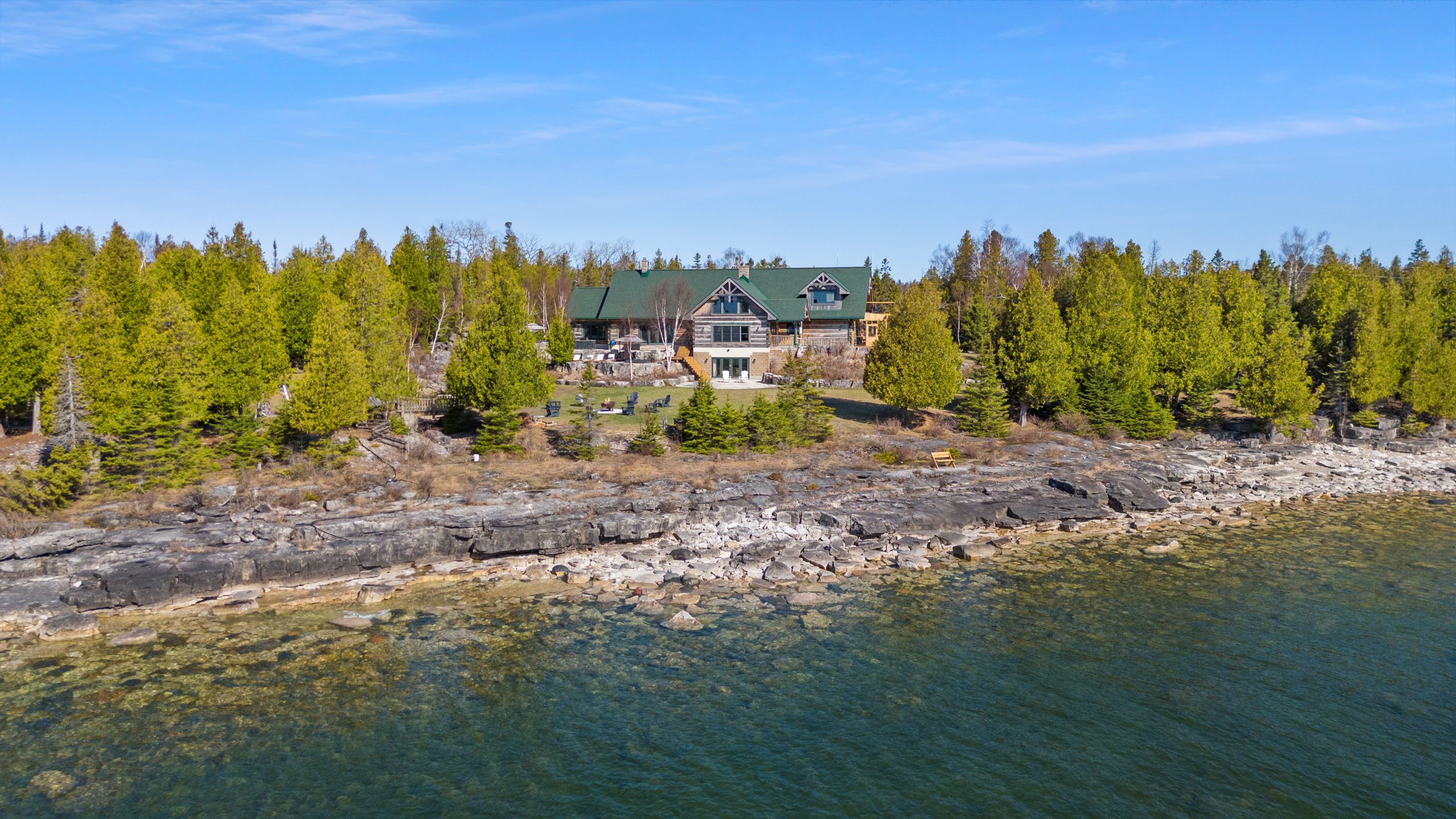 Drone view of the waterfront property at 221 Pennie Avenue on Lake Huron, with rocky shoreline and the lodge set back among trees.