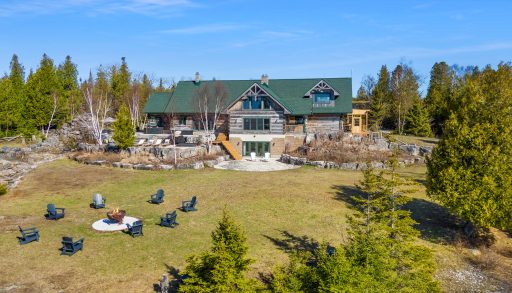 Aerial view of the main lodge and lawn at 221 Pennie Avenue, with outdoor seating and forest surrounding the property.