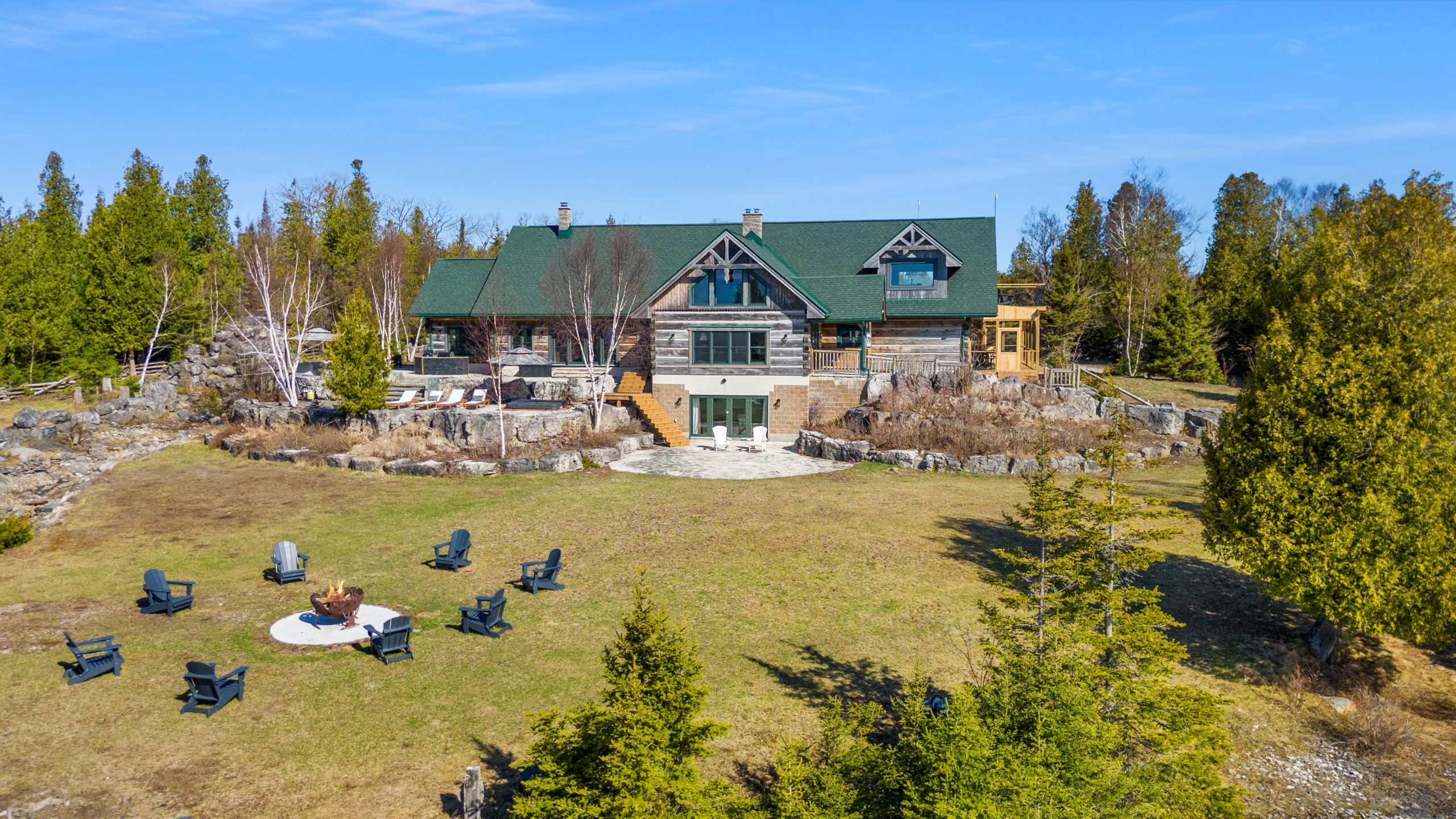 Aerial view of the main lodge and lawn at 221 Pennie Avenue, with outdoor seating and forest surrounding the property.