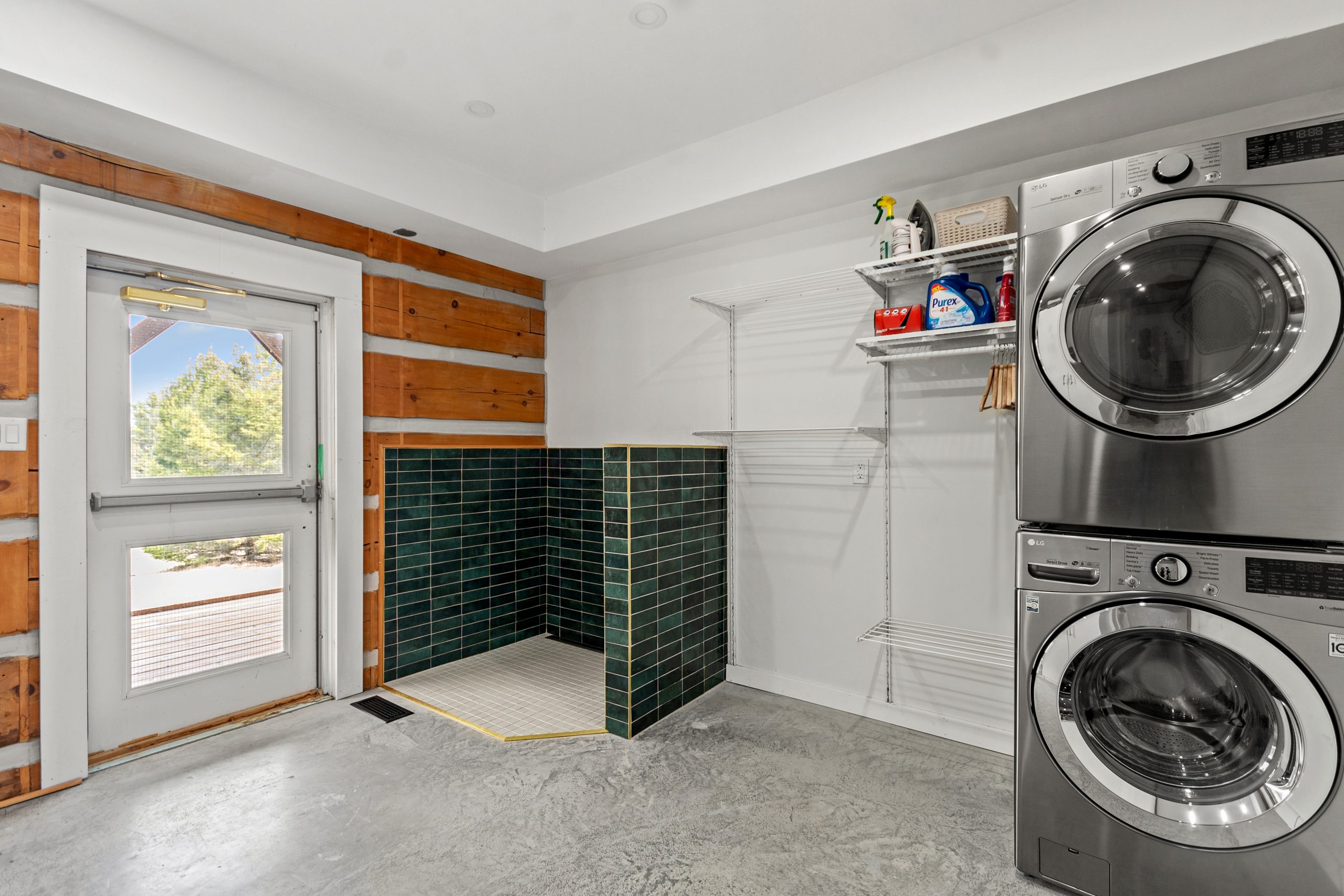Laundry area with stacked washer and dryer, concrete floors, and a door leading outside.