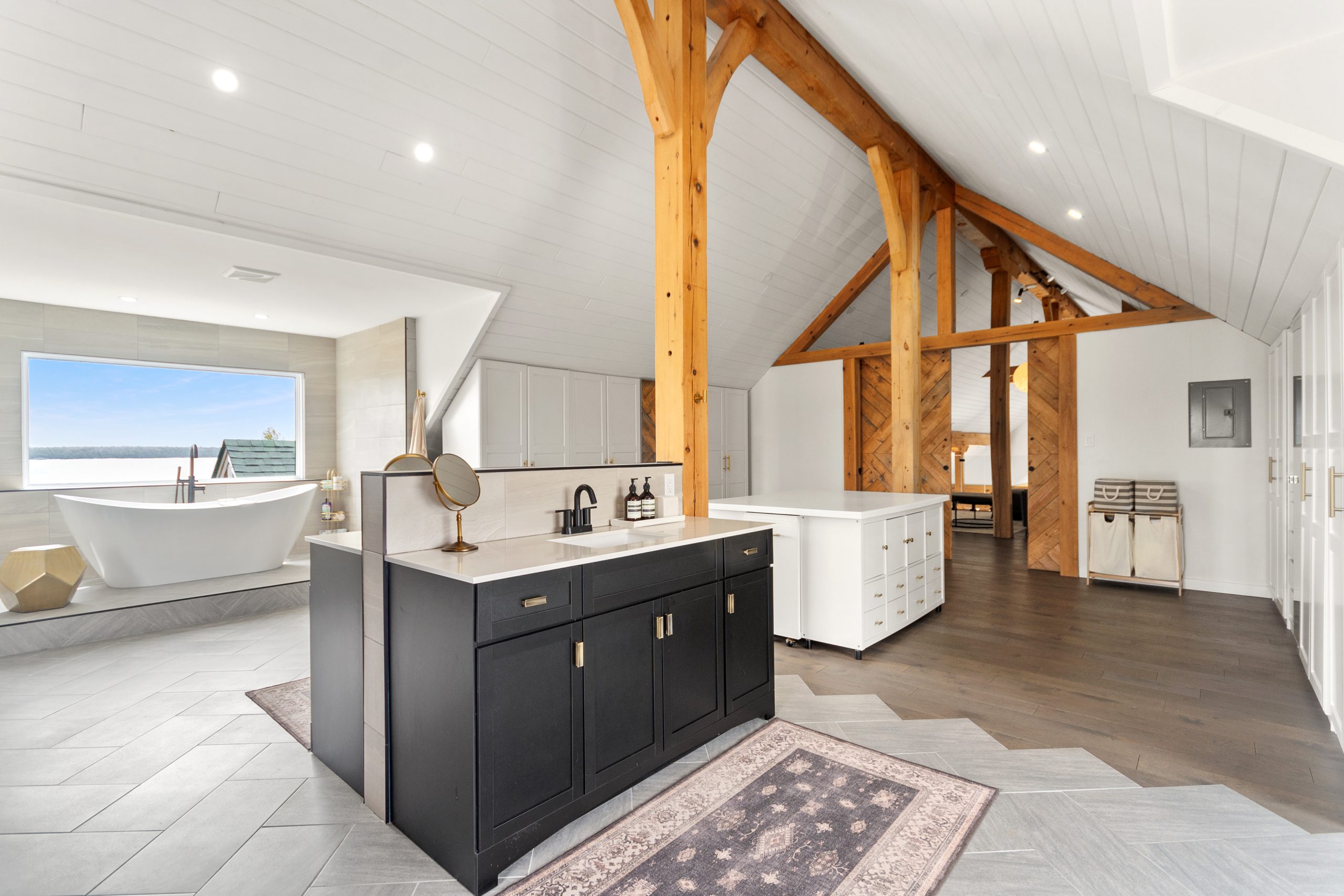 Spacious ensuite bathroom with a freestanding tub by a picture window, double vanity, and exposed timber beams.