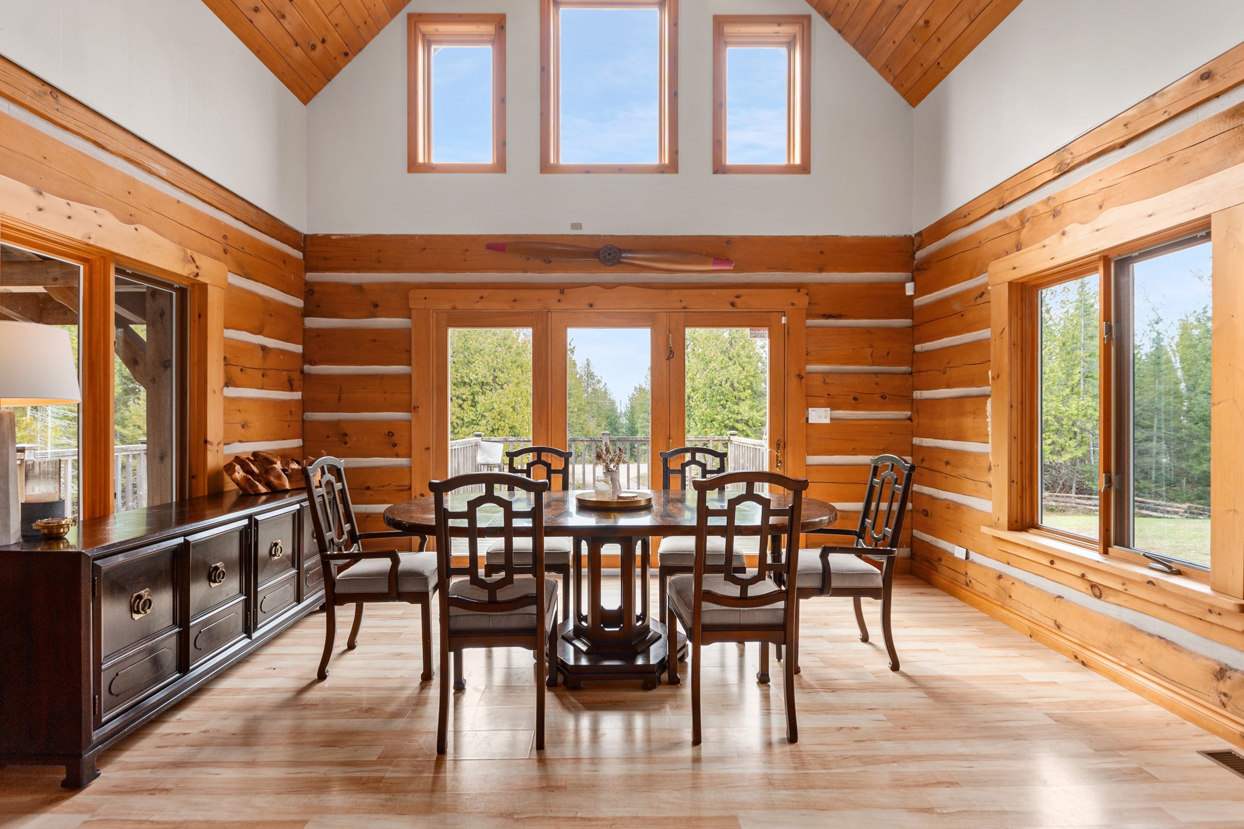 Dining area with a table and chairs, log walls, and tall windows bringing in natural light.